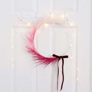 A pink pampas ombre wreath hanging on the back of a door with fairy lights